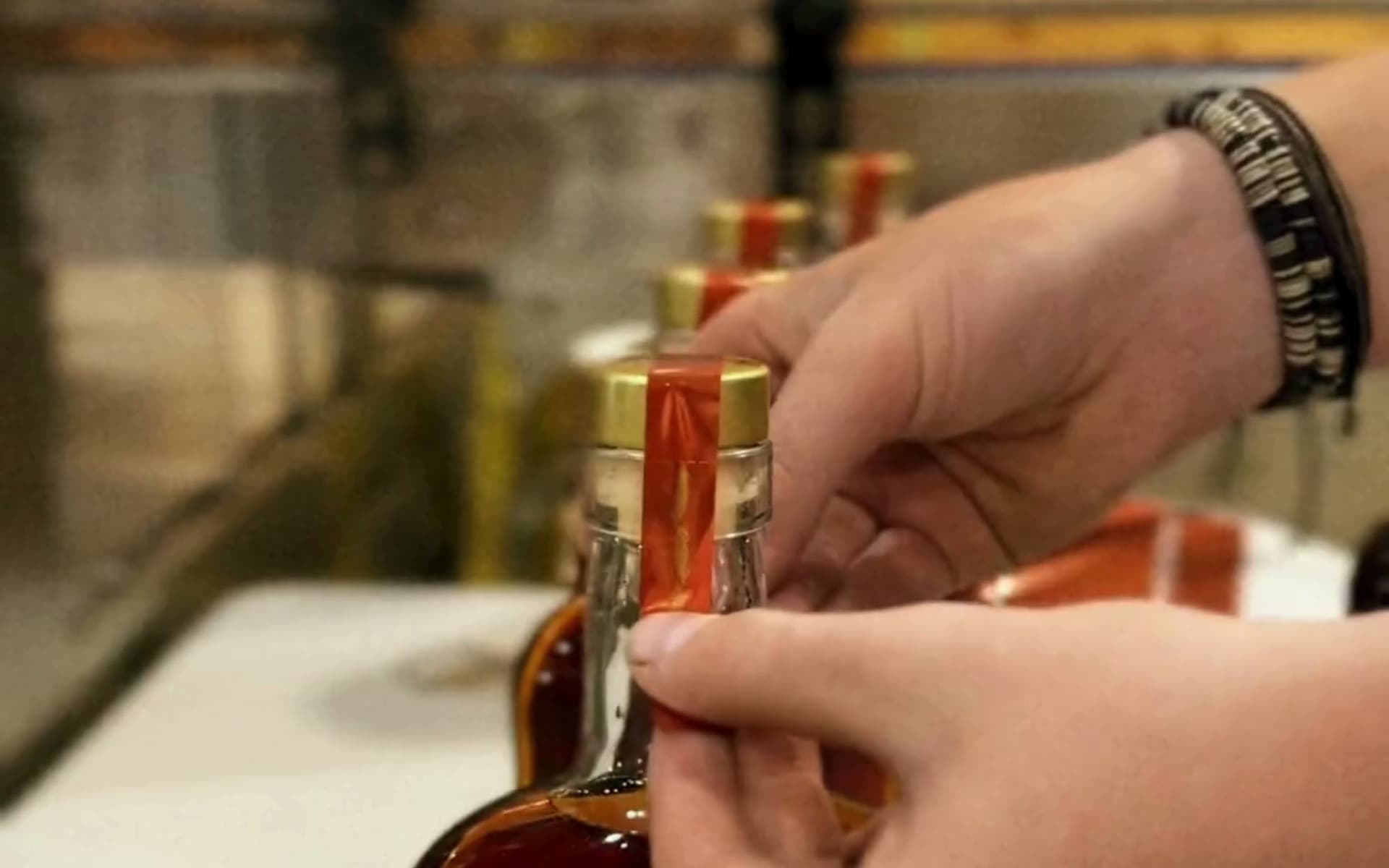 Hands applying a finishing strip to a J. Henry whiskey bottle