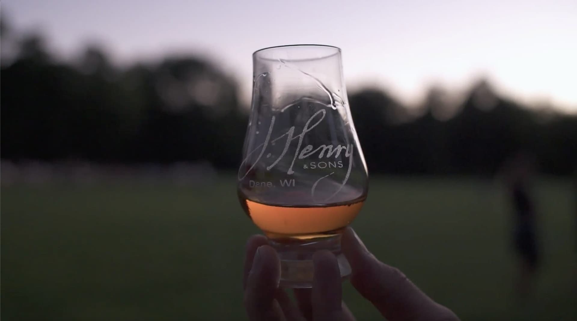 刻有 J. Henry & Sons 字樣的試飲杯,在威斯康辛黃昏的田邊舉起